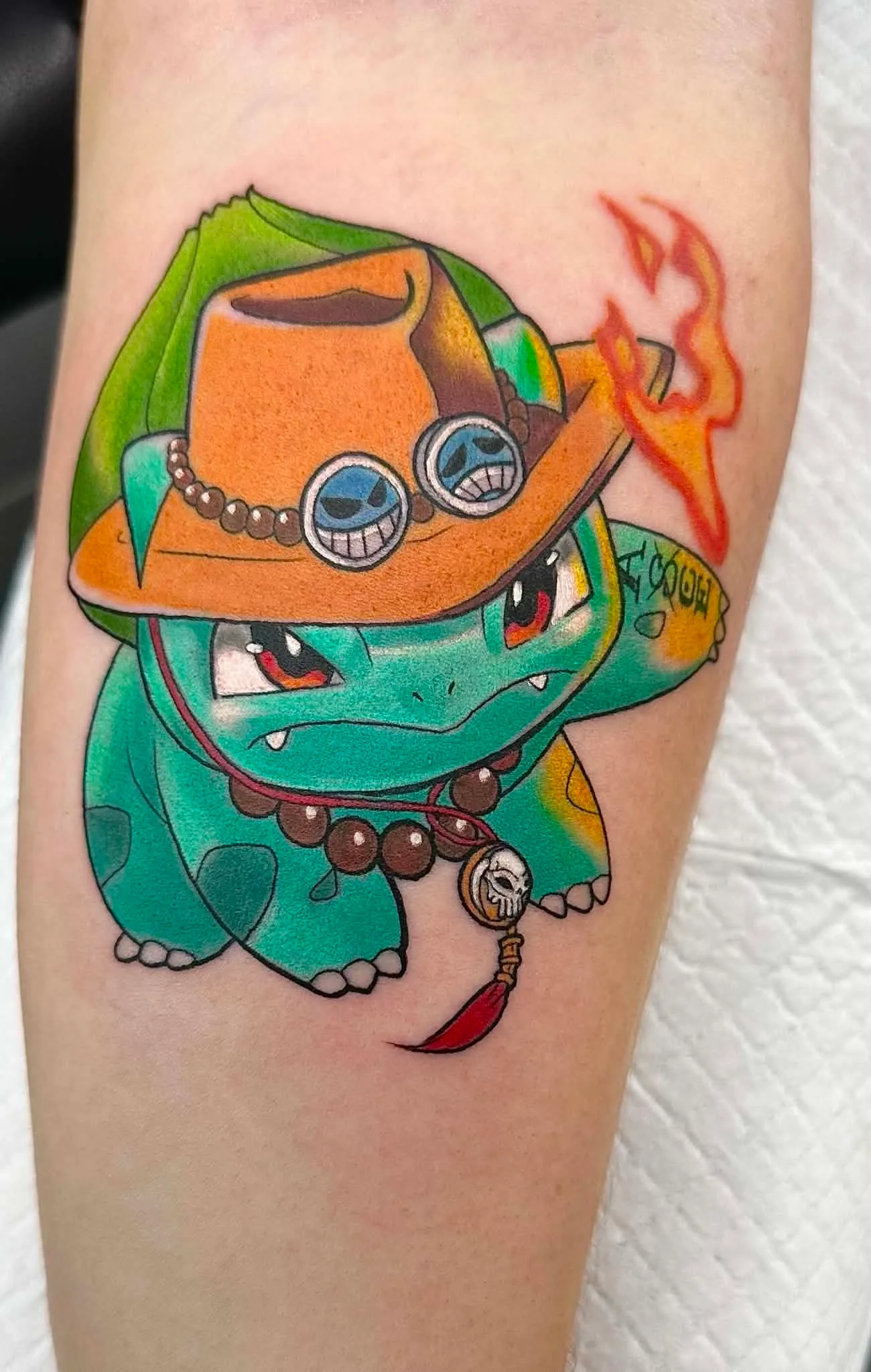 Colour tattoo of Bulbasaur wearing Portgas D. Ace hat, a One Piece and Pokemon crossover, by Crouchy